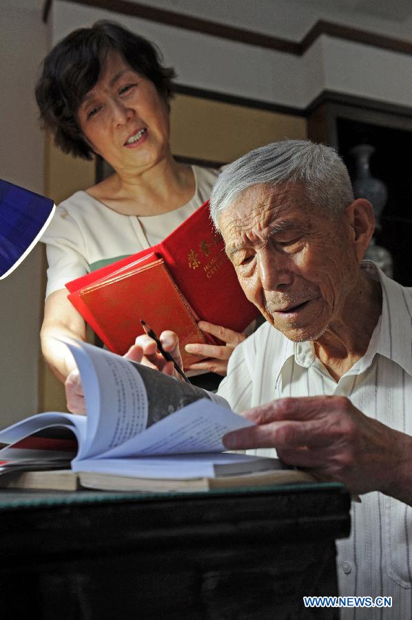 Wang Mingcai (R) reads historical records of the Chinese People's Anti-Japanese War (1937-1945) with his daughter Wang Xuehong at home in Yiwu, east China's Zhejiang Province, July 26, 2015.