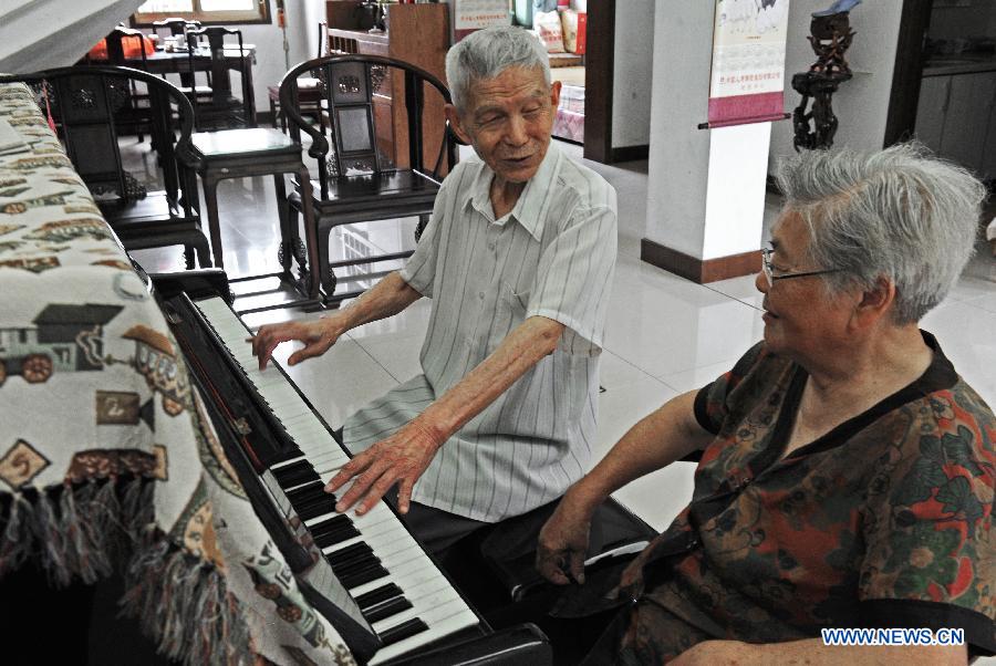 Wang Mingcai talks with his wife He Xiujuan while playing the piano at home in Yiwu, east China's Zhejiang Province, July 26, 2015. 